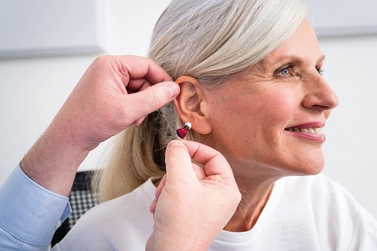 Seniorin bekommt ein modernes Hörgerät eingesetzt und lächelt bei der Hörgeräteanpassung.